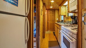 A narrow, wooden-paneled kitchen with a refrigerator, stove, and sink. - Family Cabin on 6 Acres w/ Lake Access & Hot Tub! (Springfield)