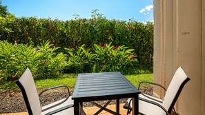 Une terrasse avec une table et deux chaises, entourée d’une végétation luxuriante et d’une haie.