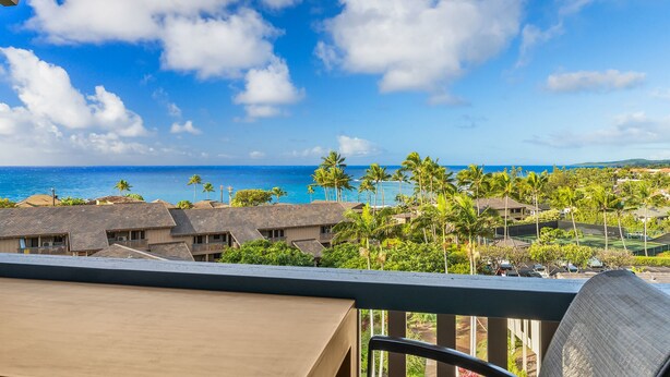 A view from a balcony overlooking a resort area with multiple buildings, palm trees, and a clear blue sky.