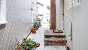 A narrow alleyway with a brick staircase leading to a door, potted plants, and a metal rack on the left side.