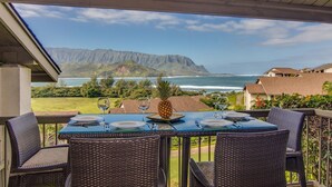 An outdoor dining area with a table set for two, overlooking a coastal view with mountains in the distance. - Aloha Condos, Hanalei Bay Resort, Condo 6303-04, Ocean View, AC (Princeville)