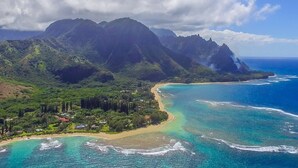 A coastal landscape with mountains, clear blue waters, and a small settlement with houses and greenery. - Aloha Condos, Hanalei Bay Resort, Condo 6303-04, Ocean View, AC (Princeville)