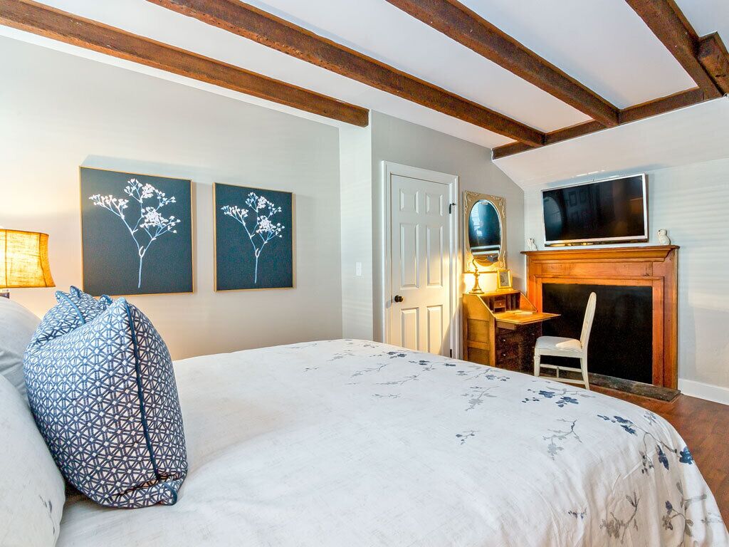 A bedroom with a bed, a desk, a television, and a fireplace.