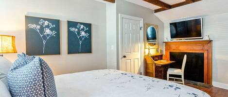 A bedroom with a bed, a desk, a television, and a fireplace.