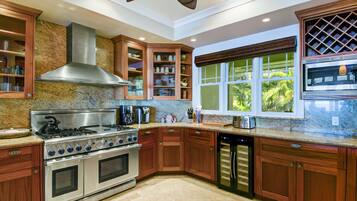 A kitchen with granite countertops, stainless steel appliances, wooden cabinets, and a large window with a view of greenery.