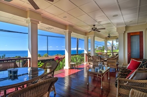 A covered outdoor area with wicker furniture, a glass table, and a view of the ocean.