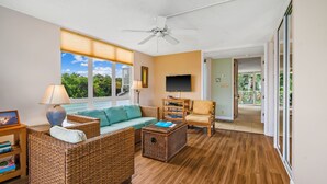 Un salón con muebles de mimbre, un ventilador de techo, un televisor y vistas al exterior.