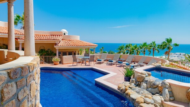 A pool area with lounge chairs and a view of the ocean.