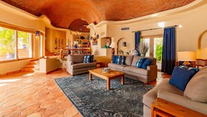 A spacious living area with a high, curved brick ceiling, a large window with a view of greenery, and a cozy seating arrangement with sofas and a coffee table.