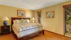 Une chambre à coucher comprenant un lit, deux tables de chevet avec des lampes, une fenêtre avec des stores et deux tableaux floraux encadrés accrochés au mur.