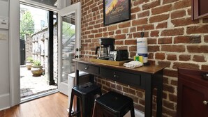 A kitchen with a brick wall, a coffee machine, and two stools. - Garden Level Steps from Shops and Restaurants by Lucky Savannah (Savannah)