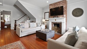 A living room with a fireplace, a staircase, and a television mounted above it. - Garden Level Steps from Shops and Restaurants by Lucky Savannah (Savannah)