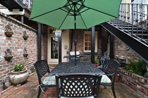 Een terras met een tafel, stoelen, een groene parasol en bakstenen muren.