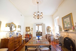 Une salle à manger avec une longue table, des chaises, un lustre, une cheminée et un miroir doté d’un cadre doré.
