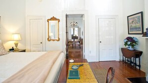 Une chambre d’hôtel comprenant un lit, un bureau avec une lampe, une chaise, un miroir et une porte donnant sur un coin repas.