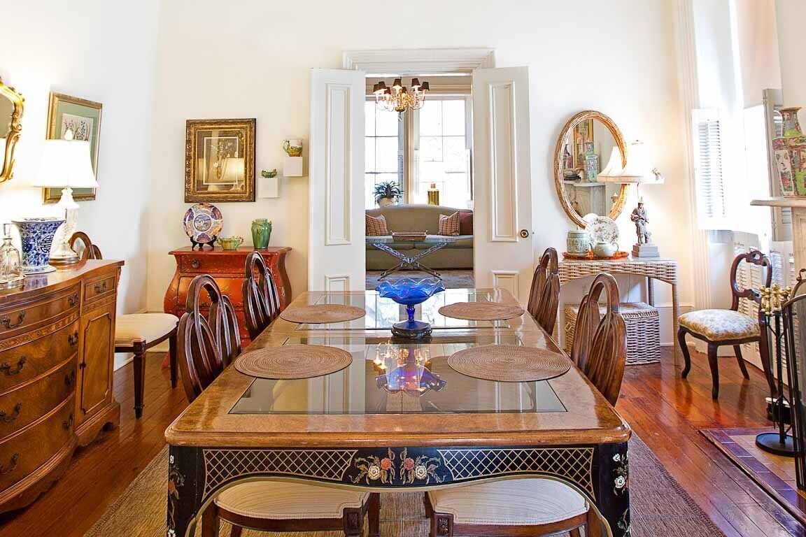 A dining room with a glass-top table, wooden chairs, and a view into a living area through an open door.