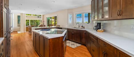 A modern kitchen with wooden cabinets, a central island, and a view of the outdoors.
