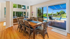 A dining area with a wooden table and wicker chairs, large windows, and a view of a swimming pool. - Kiahuna Vista by Parrish Kauai - Private Pool and AC (Koloa)