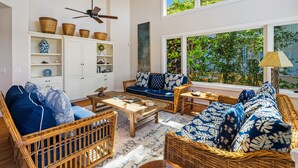 A living room with wicker furniture, a ceiling fan, and a view of greenery through large windows. - Kiahuna Vista by Parrish Kauai - Private Pool and AC (Koloa)
