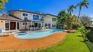 Una casa de dos pisos con piscina, mobiliario de patio y un jardín trasero cercado.