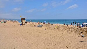 A beach with a lifeguard tower, umbrellas, and people relaxing. - 1005 E. Balboa A | Gorgeous Oceanfront w/ HUGE patio (Newport Beach)