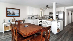 A modern kitchen with white cabinetry, a wooden dining table, and a painting on the wall. - 1005 E. Balboa A | Gorgeous Oceanfront w/ HUGE patio (Newport Beach)