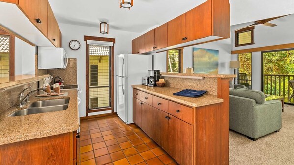 A compact kitchen with wooden cabinets, a sink, and a refrigerator. There is a window with a view of greenery outside.