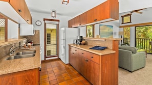 Enjoy cooking and relaxing in this well-designed kitchen and living area with a comfortable sofa and balcony overlooking lush greenery.