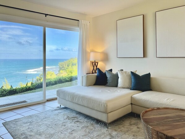 A modern living room with a large sliding glass door leading to a balcony with a view of the ocean.