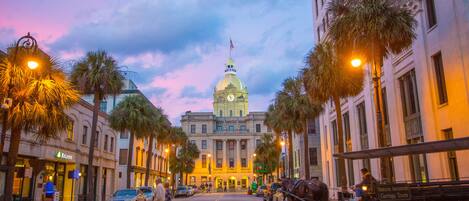 A street with a horse-drawn carriage, palm trees, and a building with a dome and flag.