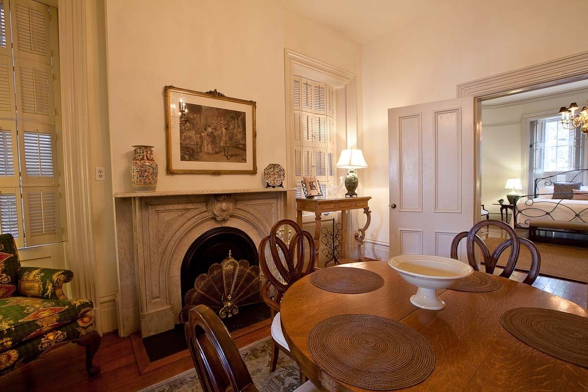 A dining room with a fireplace, a table with placemats, chairs, a lamp, and a framed picture on the wall.
