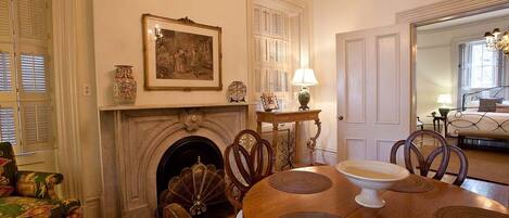 A dining room with a fireplace, a table with placemats, chairs, a lamp, and a framed picture on the wall.