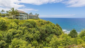 A multi-story hotel with balconies overlooking a coastal area, surrounded by lush greenery and palm trees. - Expansive Ocean Views from Ali'i Kai 5103 (Princeville)