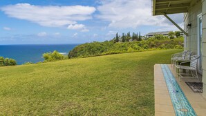 A pool area with a view of the ocean, a grassy slope, and a building with a covered patio. - Expansive Ocean Views from Ali'i Kai 5103 (Princeville)
