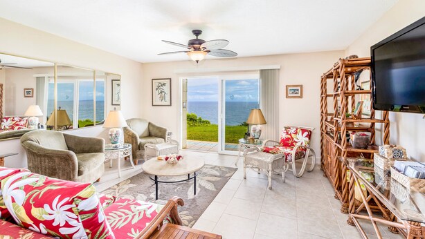A spacious living room with a large TV, comfortable seating, a ceiling fan, and a view of the ocean through large windows. - Expansive Ocean Views from Ali'i Kai 5103 (Princeville)