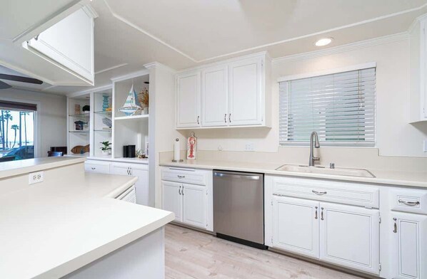 Una cocina moderna con armarios blancos, lavavajillas y una ventana con persianas.