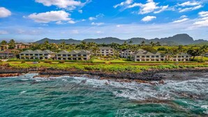 Un hotel costero con varias construcciones, un litoral rocoso y vistas a montañas al fondo.