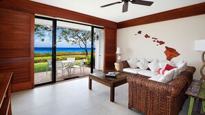A room with a view of the ocean, a wicker sofa, a table, and a ceiling fan.