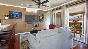 A living room with a ceiling fan, a flat-screen TV, a sofa, a dining area with chairs, and a view of a balcony with outdoor furniture. - Nalo Studio A By Parrish Kauai - local vibe & walk to Poipu Beach (Koloa)