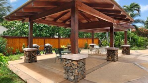 An outdoor patio with a wooden pergola, stone pillars, and outdoor furniture.