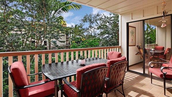 Ein Balkon mit Tisch und Stühlen, eine Glastür, die in einen Innenbereich führt, und im Hintergrund Blick auf Grünflächen und Gebäude.