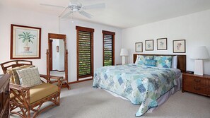 Ein Schlafzimmer mit Bett, Stuhl, Nachttisch, Lampe, Deckenventilator und einer Tür mit Blick auf Grünflächen.