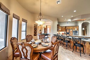 A spacious dining area with a large round table, multiple chairs, and a central chandelier.