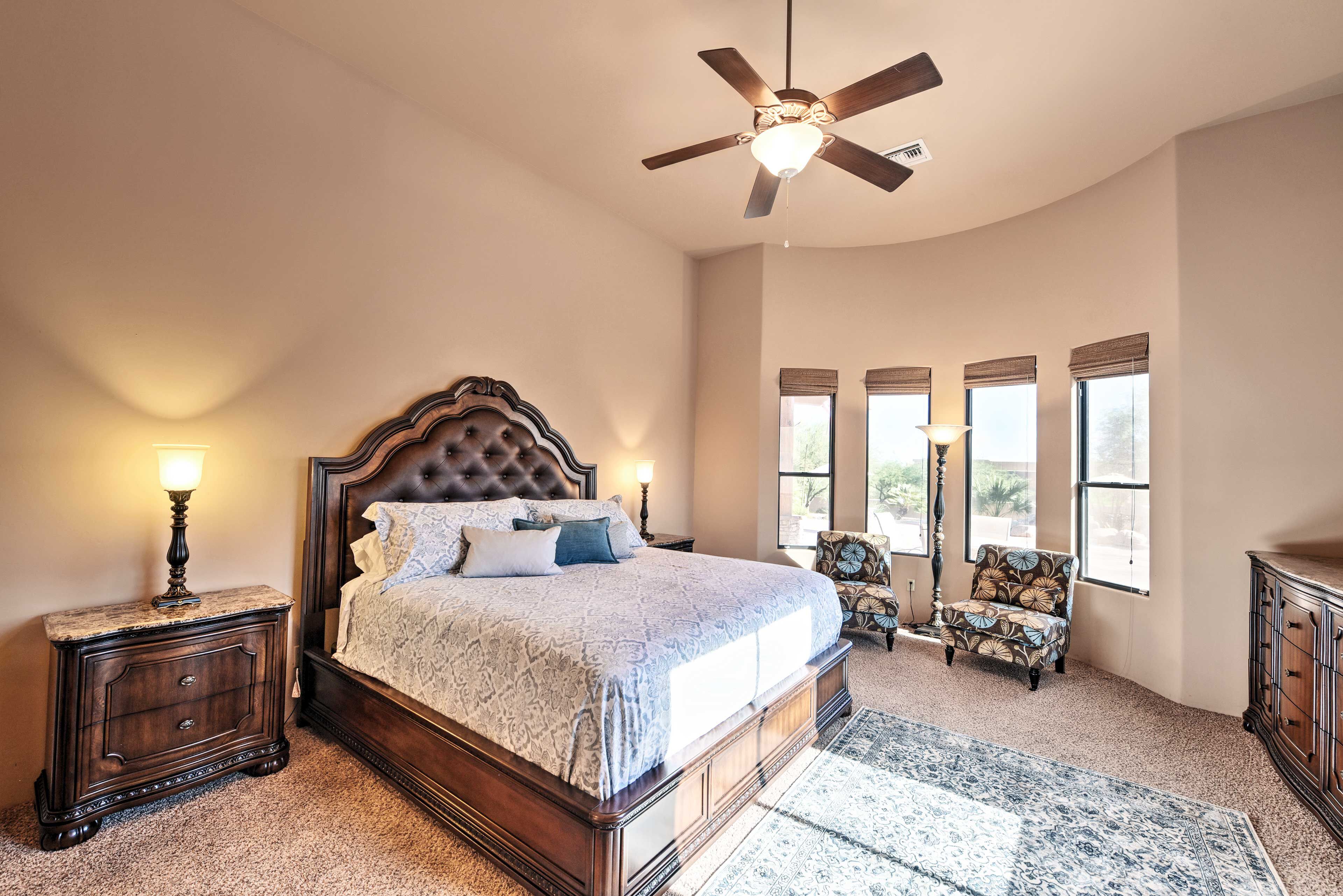 A bedroom with a large bed, a ceiling fan, a nightstand, a chair, and a dresser.