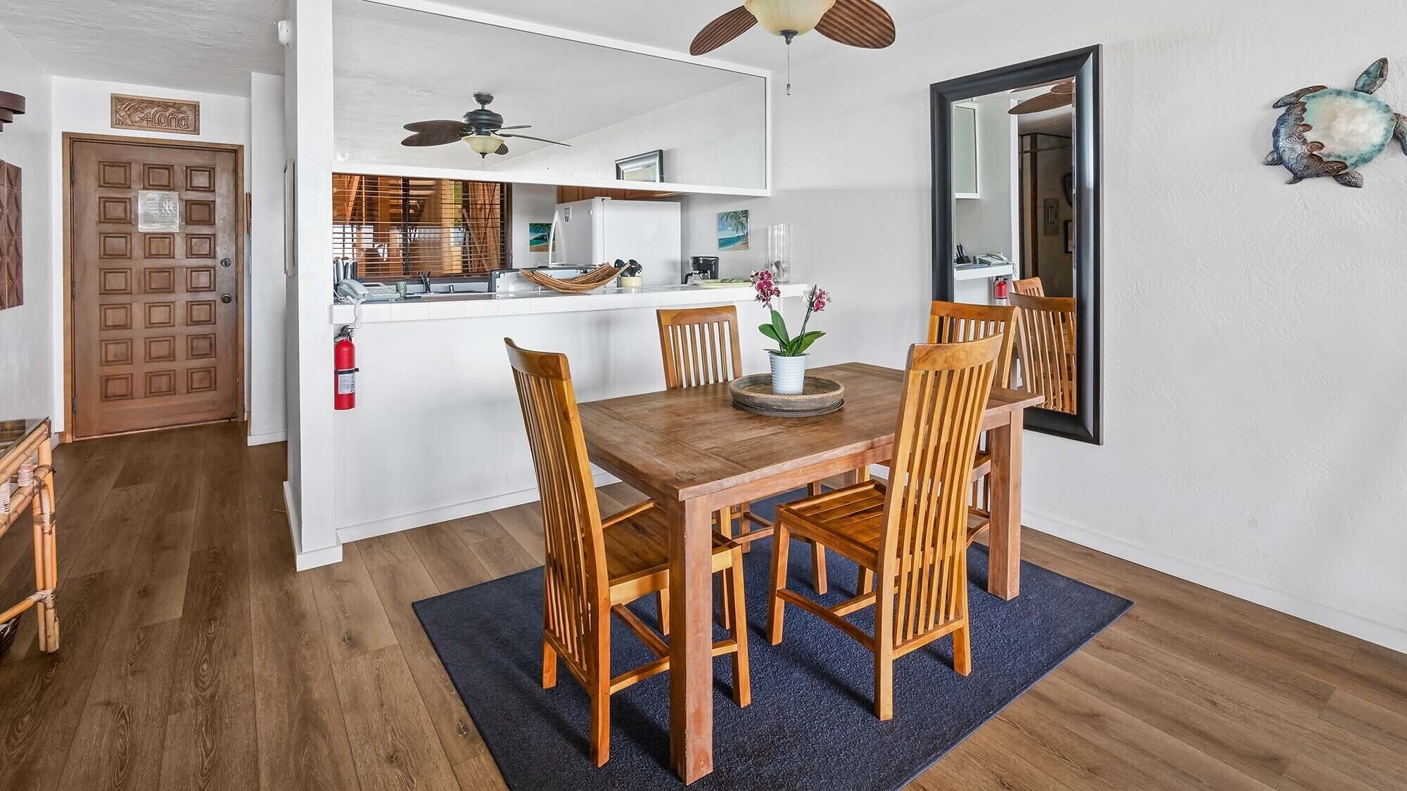 Un comedor con una mesa y sillas de madera, un ventilador de techo y una cocina con refrigerador y espacio en la encimera.
