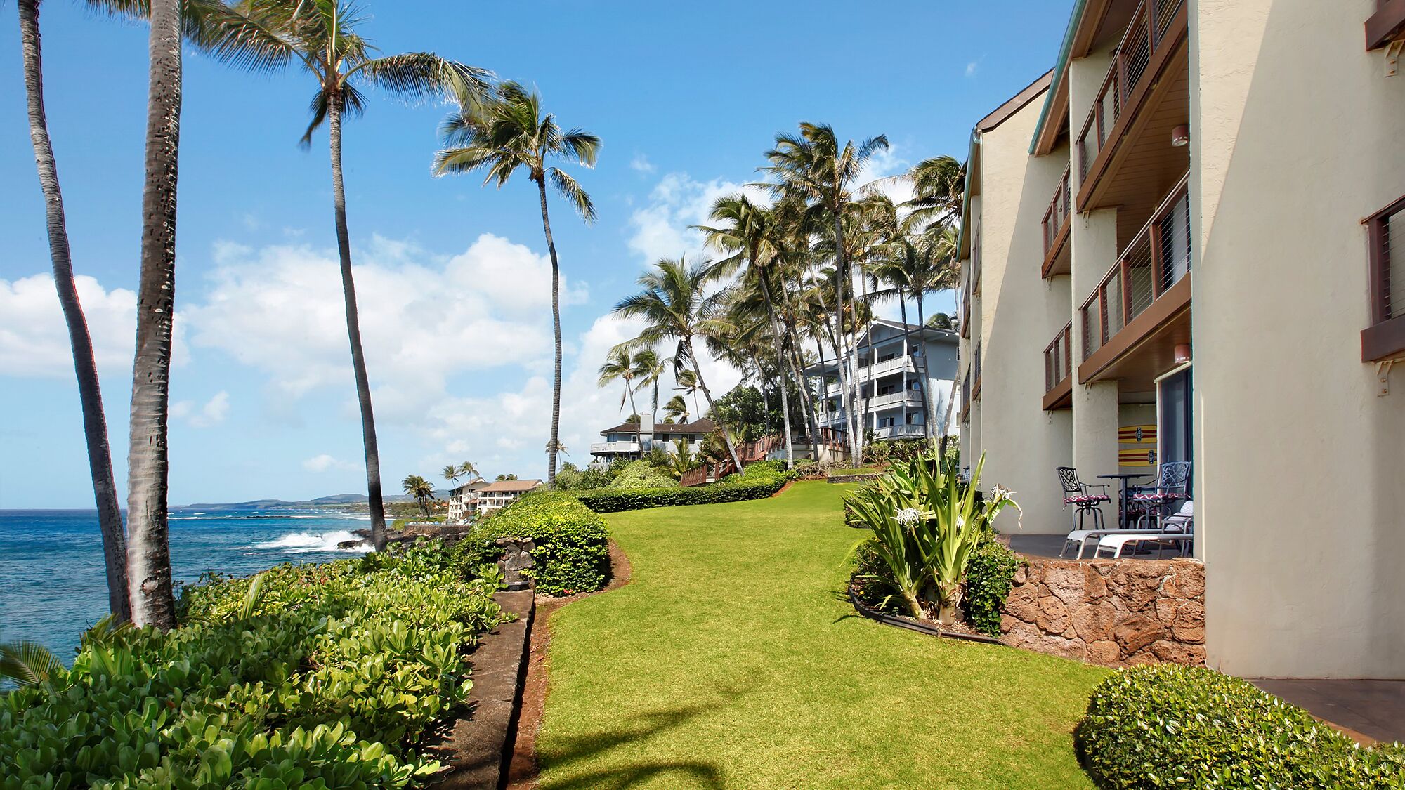 A beachfront hotel with a well-maintained lawn, palm trees, and ocean views.