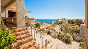 Un escalier menant à une terrasse d’où l’on peut admirer la mer, le tout étant entouré de bâtiments et de verdure.