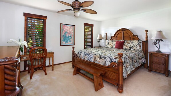 Un dormitorio con cama de madera, ventilador de techo, mesita de noche, una silla y ventana con contraventanas.