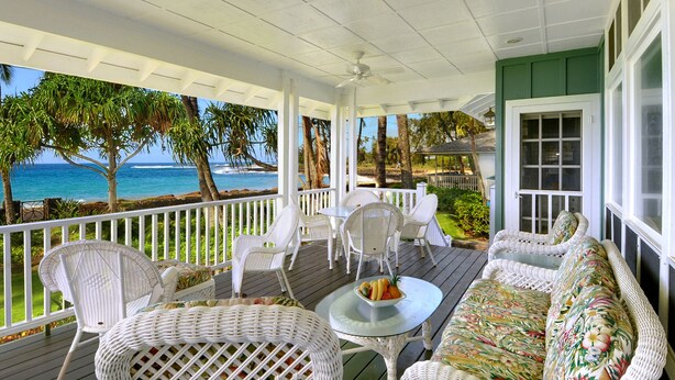 A covered porch with wicker furniture, a glass table, and a view of the ocean.