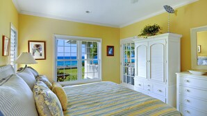 A bedroom with a bed, a dresser, a lamp, and a view of the ocean through a large window.